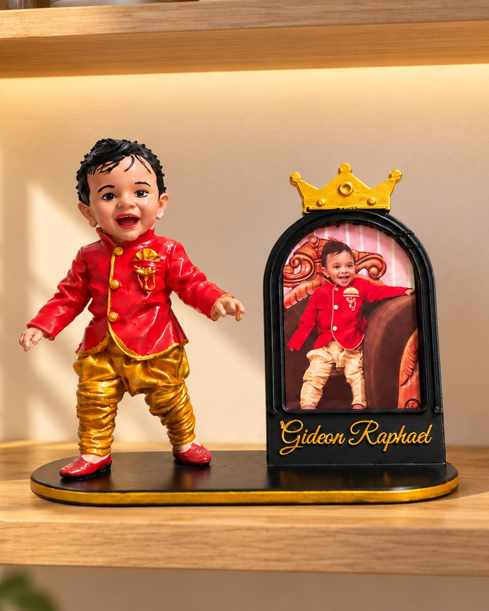 Personalised baby miniature figurine in red jacket and gold pants beside a crown photo frame with name, front view